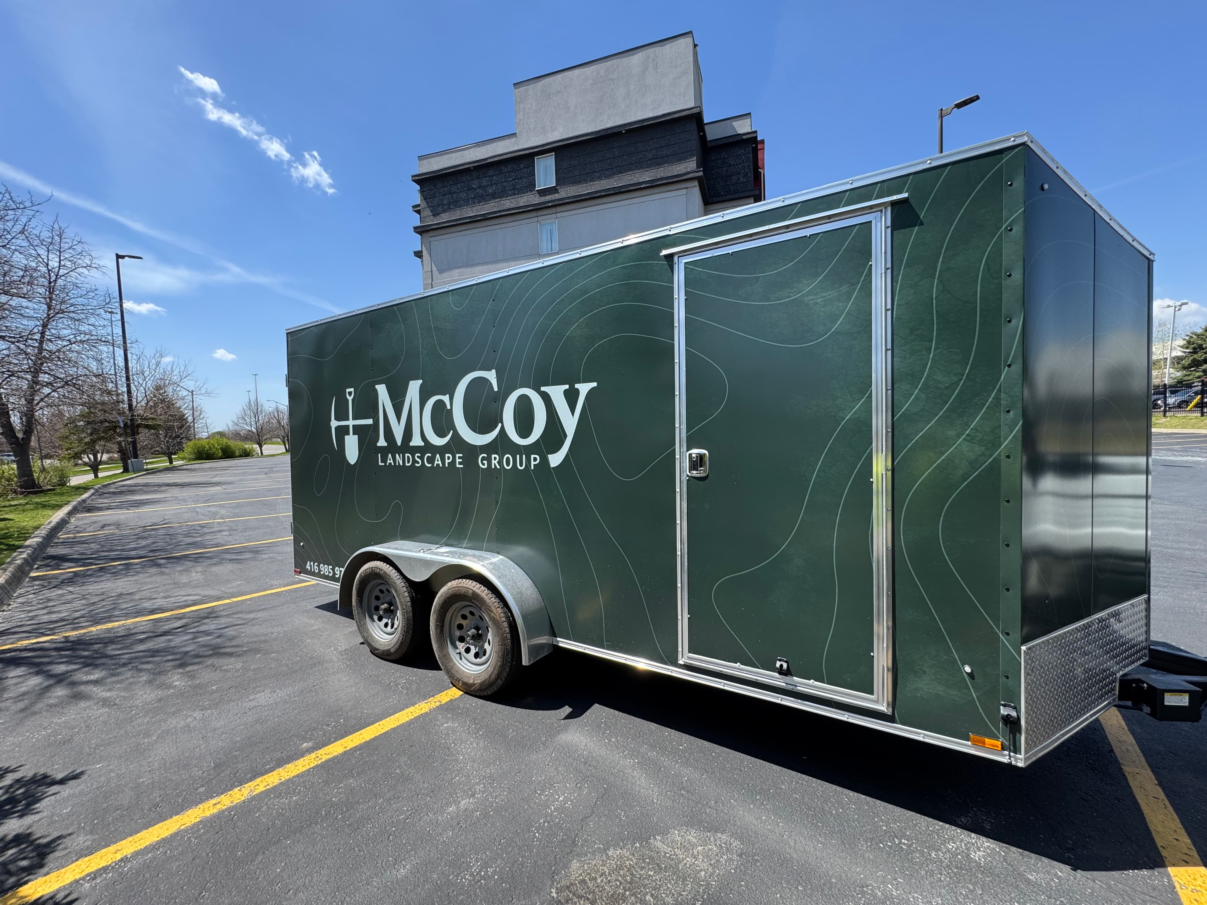 McCoy Landscape Group wrapped trailer with topographic-line branding, parked on a West GTA job site