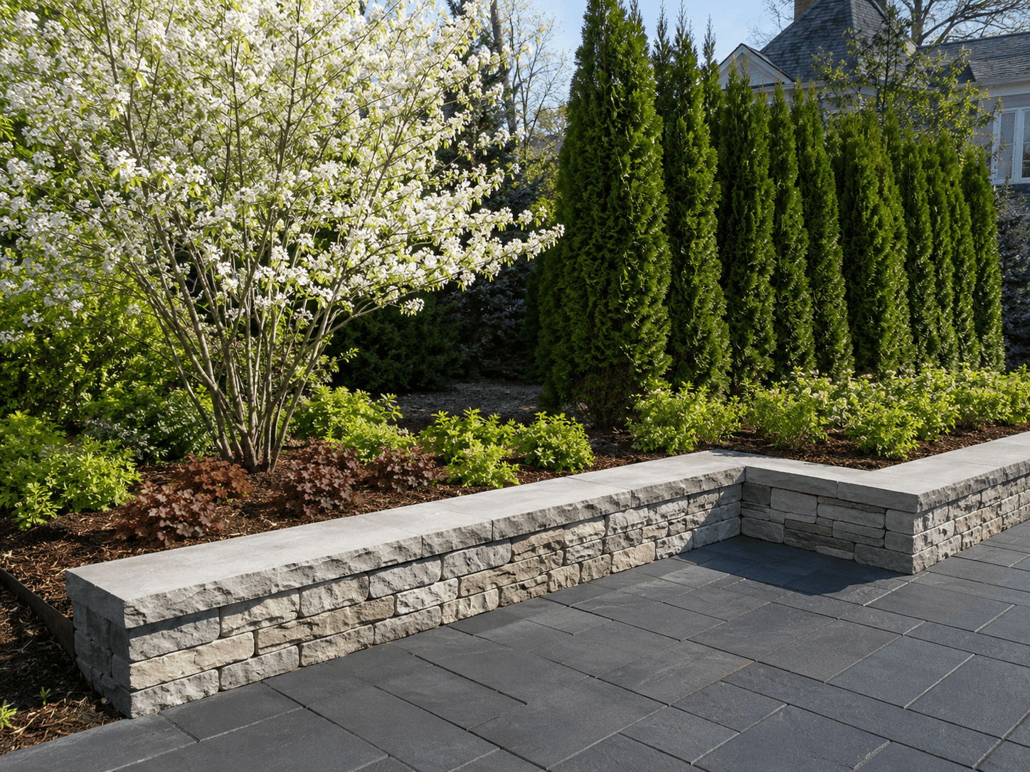 New garden beds, trees, and shrubs planted to frame a patio and seating wall in Oakville by McCoy Landscape Group